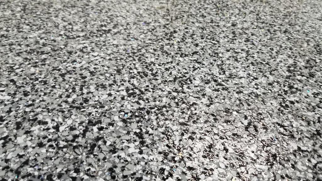 Fully remodeled domino epoxy shop floor complete with gray, white and black chips evenly spread and coated with a clear and shiny enamel top coat.