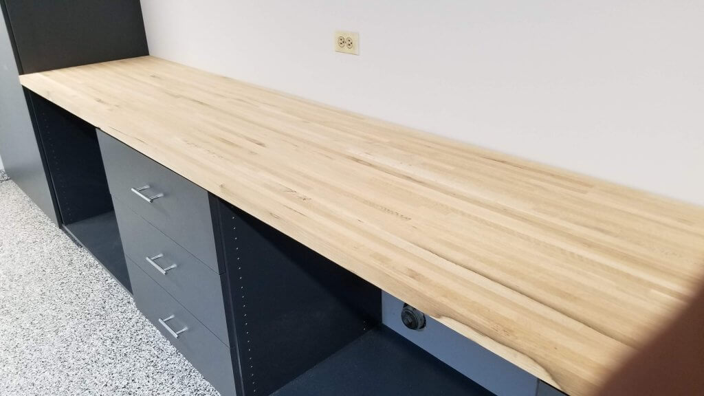 12 foot long raw maple workbench installed in makerspace on top of lower garage cabinet set.