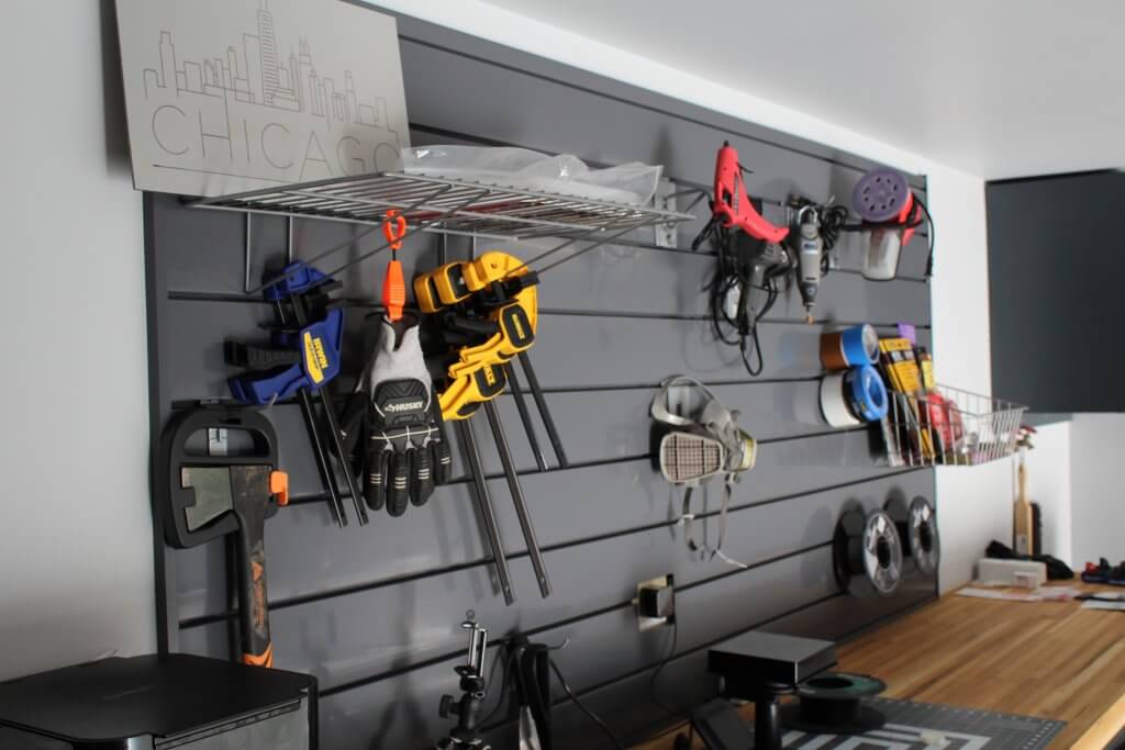 Fully remodeled slat wall mounted above the shop's workbench shown with brackets installed and various tools and materials hanging from them for the makerspace.