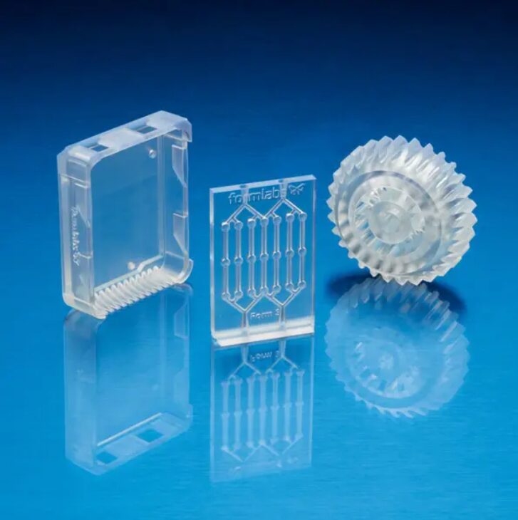 Three clear objects 3D printed out of Formlabs Clear resin are shown sitting against a blue background.