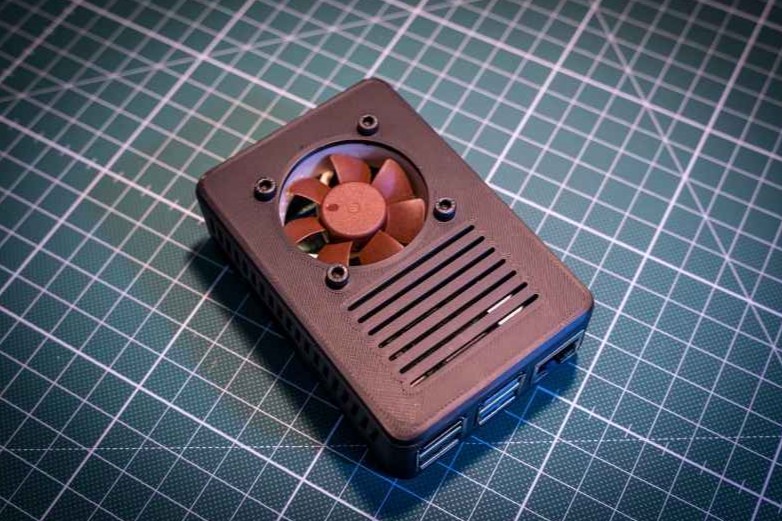 A brown fan enclosure, 3D printed out of ABS material, is shown sitting atop a grid-lined surface.