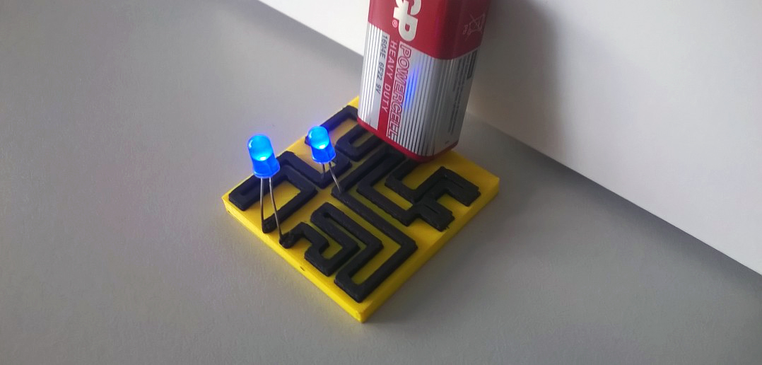 A simple LED circuit is shown 3D printed out of conductive filament. A battery is held against the positive and negative poles of the circuit, as the blue LED's on either end of the circuit light up simultaneously.