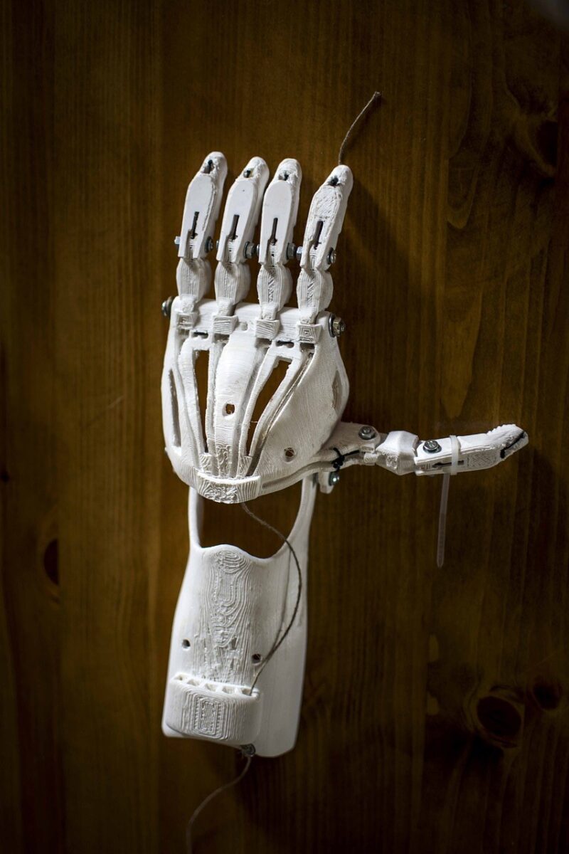 A white, 3D printed, prosthetic hand is shown lying atop a wooden surface.